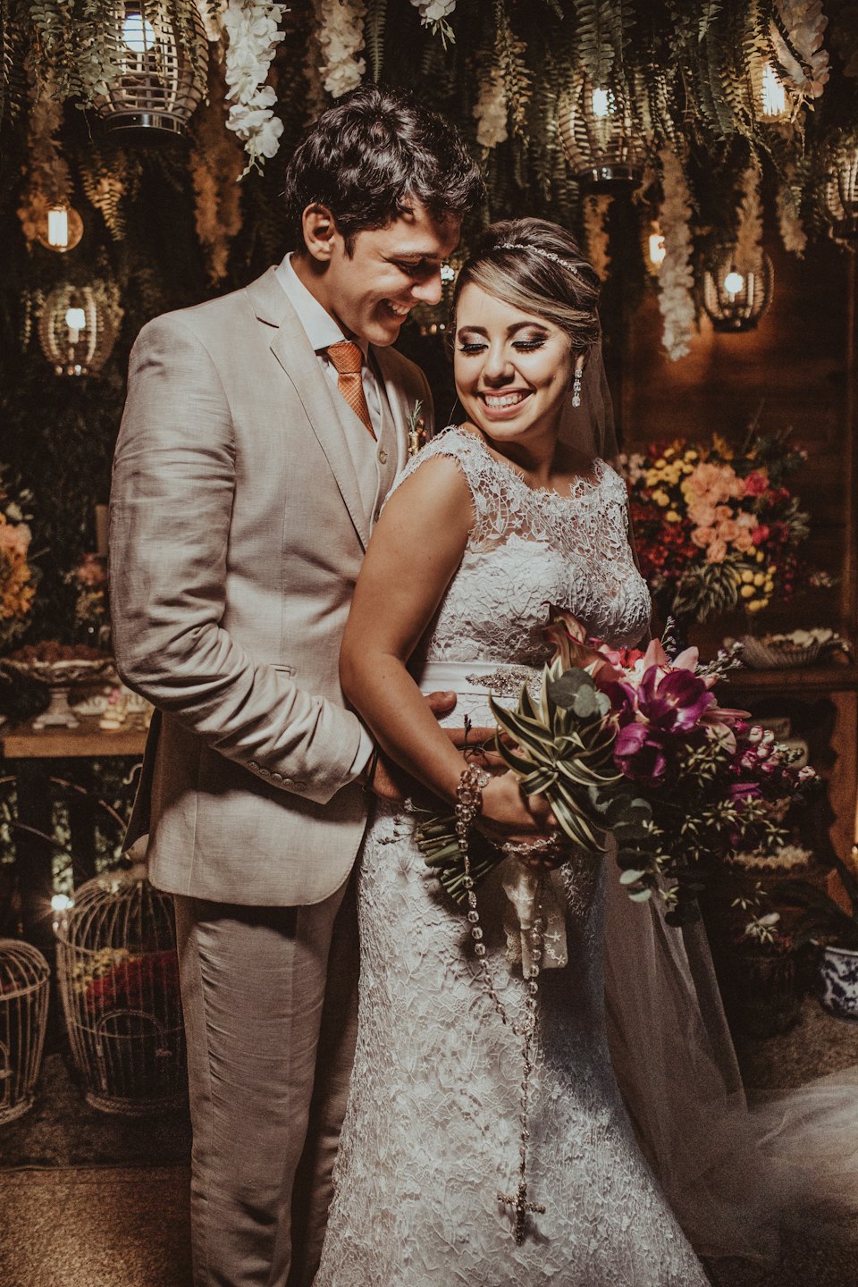 A wedding couple embraces while surrounded by hanging lanterns and flowers.